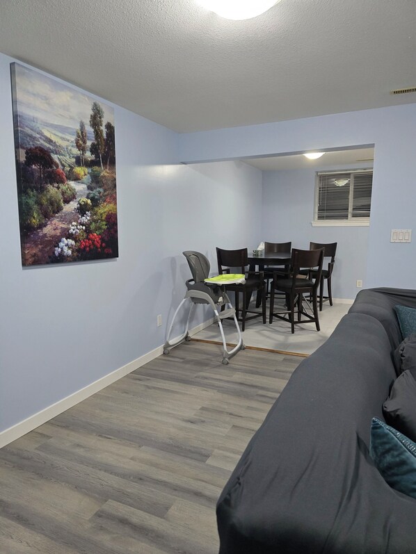 A room with a dining area, a gray sofa, and a painting on the wall.