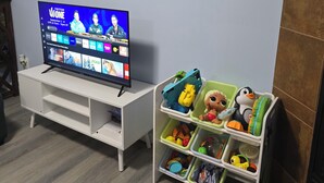 A room with a TV on a white stand, a storage unit with toys, and a wooden floor. - Private 2 bedroom basement suite in Langley (Langley)