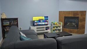 A living room with a flat-screen TV on a white stand, a bookshelf, a fireplace, and a sofa. - Private 2 bedroom basement suite in Langley (Langley)