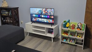 A room with a TV on a white stand, a bed, a small wooden shelf with books, and a toy storage unit. - Private 2 bedroom basement suite in Langley (Langley)
