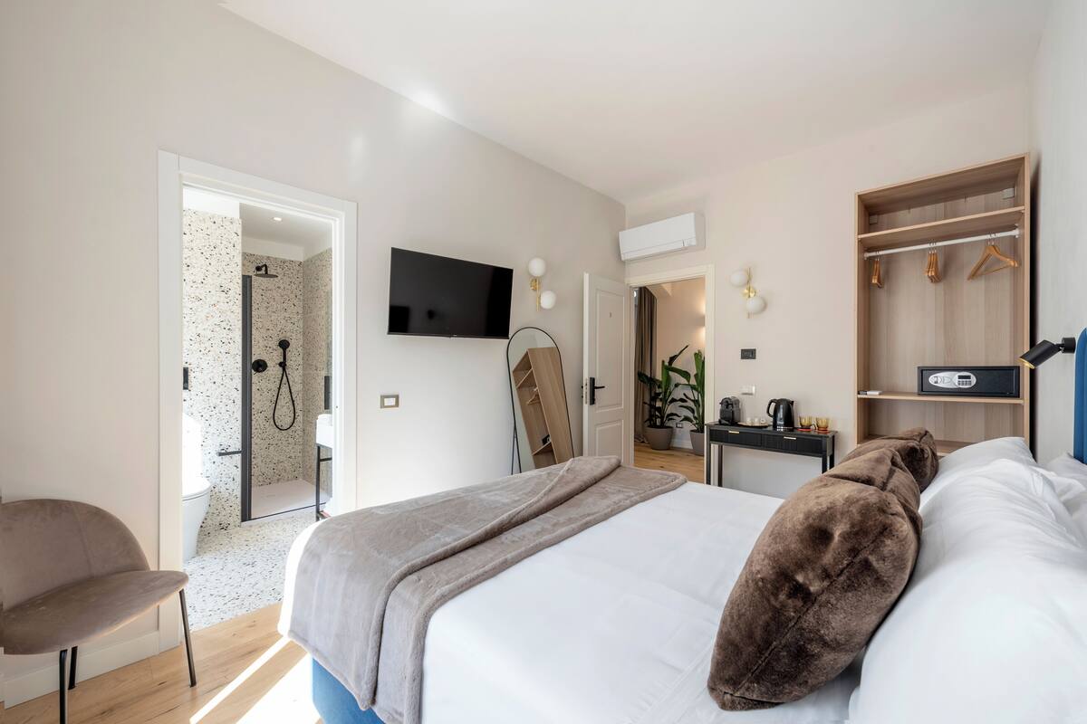 A modern bedroom with a large bed, a TV mounted on the wall, a walk-in closet, and a shower area.