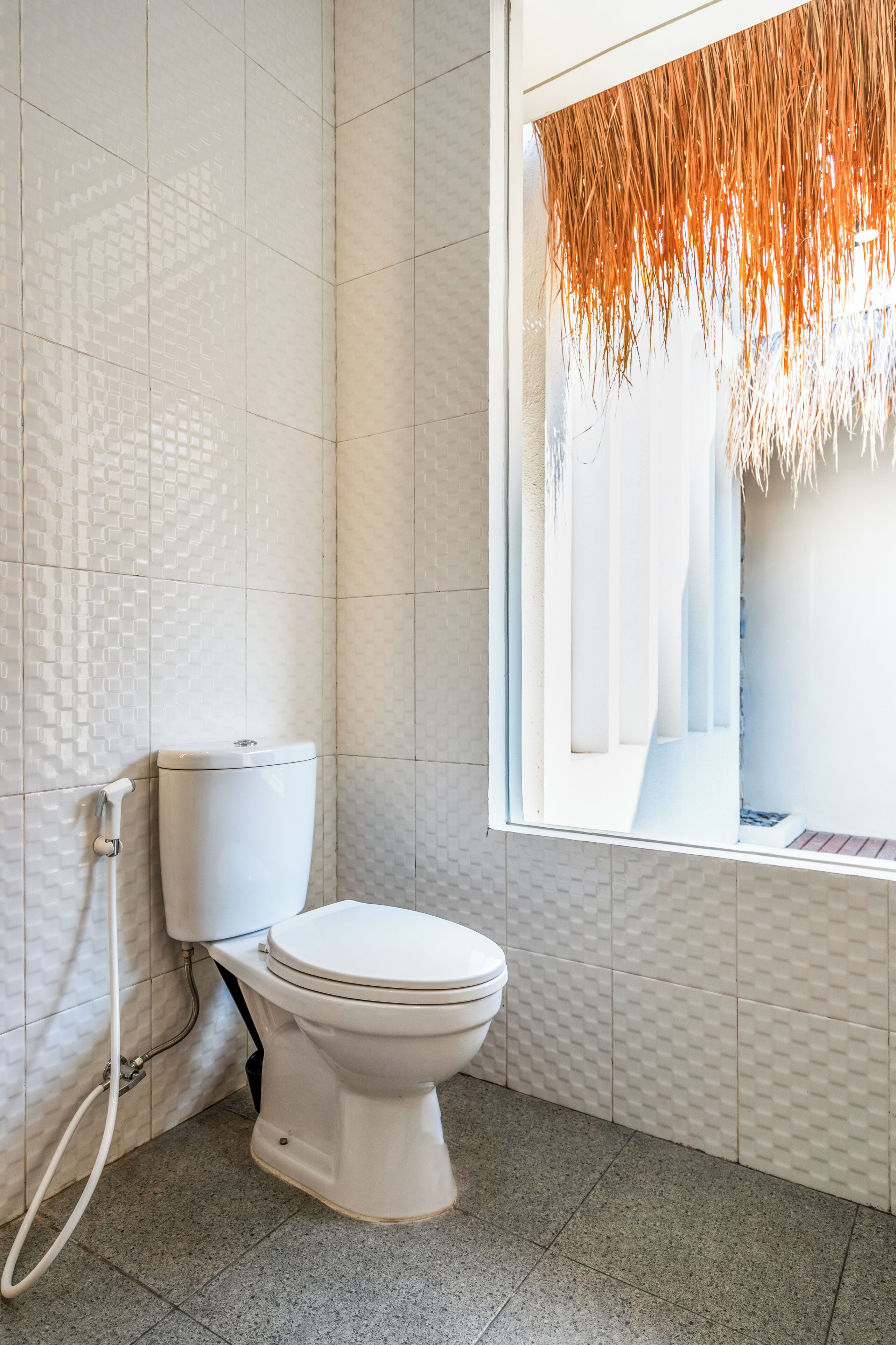 A modern bathroom with a white toilet, tiled walls, and a window with a textured curtain.