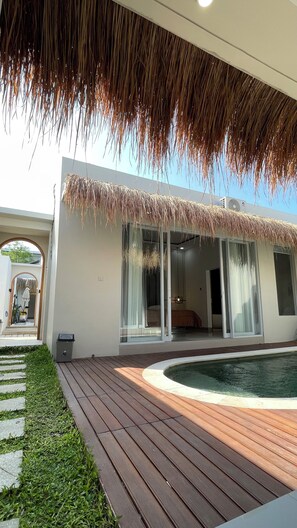A modern house with a pool, a wooden deck, and a thatched roof.