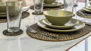 Un'area pranzo moderna con un tavolo in vetro, ciotole verdi e bicchieri trasparenti su sottopiatti in fibra naturale.