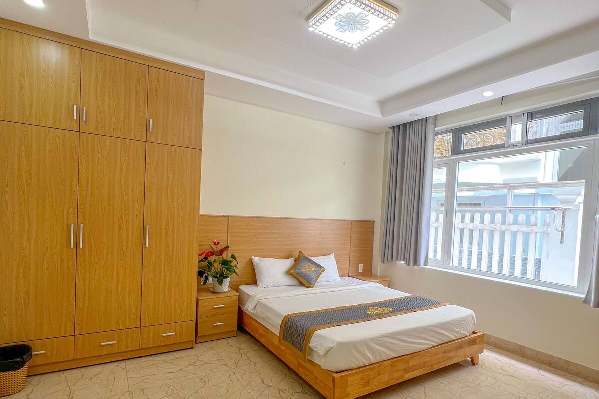 A bedroom with a bed, wooden wardrobe, and a window with a view.