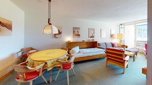 Une pièce confortable avec un lit, une table à manger et des chaises. Les murs sont ornés de tableaux et une fenêtre laisse entrer la lumière naturelle.