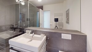 Une salle de bain moderne avec un grand miroir, un lavabo et un espace douche.
