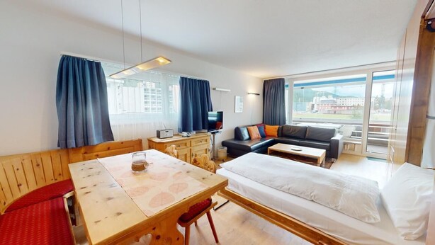 A hotel room with a wooden dining table, a sofa with cushions, a bed, and a TV. - Well-kept holiday apartament house in a prime location in St. (St. Moritz)