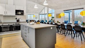 A modern kitchen with a central island, built-in ovens, and a dining area with yellow pendant lights and a view of the outdoors. - 16 Person Holiday Home in Sydals (Sydals)