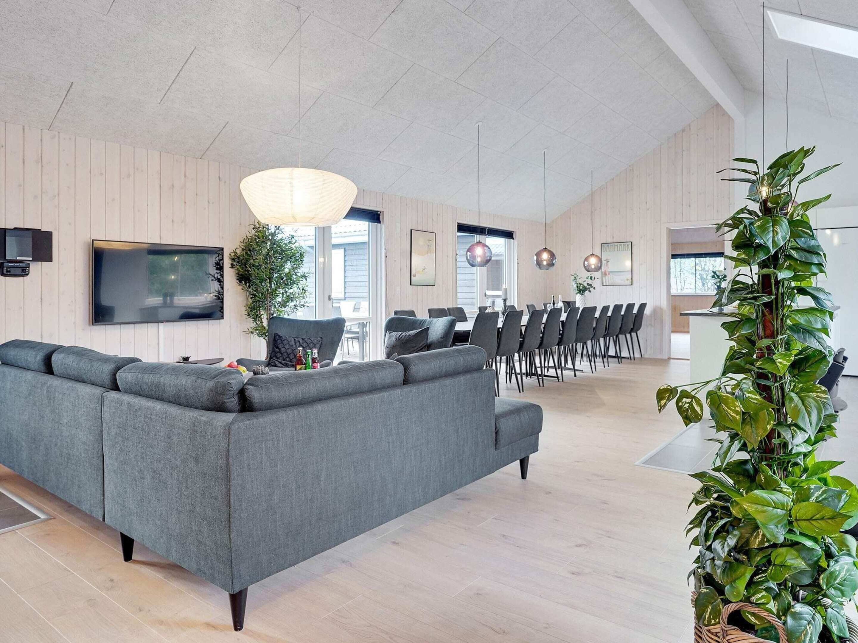 A modern living room with a grey sectional sofa, a large hanging light fixture, and a dining area with chairs and a table.