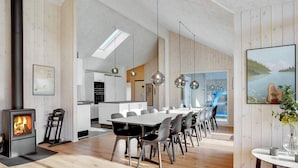 A modern kitchen with a central island, a dining area with a long table and chairs, and a large window with a view of a lake. - 16 Person Holiday Home in Sydals (Sydals)