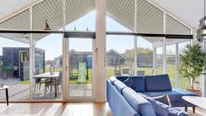 A modern interior with a large glass door leading to an outdoor area, a blue sofa, and a dining table. - 16 Person Holiday Home in Sydals (Sydals)