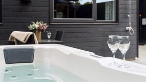 Un bain à remous extérieur moderne, avec deux verres d’eau, une table et une chaise devant.