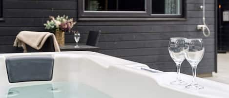 Een moderne bubbelbad buiten, met twee glaasjes water, een tafel en een stoel ervoor.