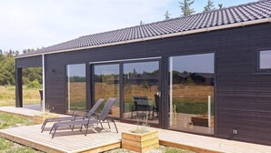 Une maison moderne dotée d’une grande porte vitrée, d’une terrasse avec deux chaises longues et d’une vue sur le paysage environnant.