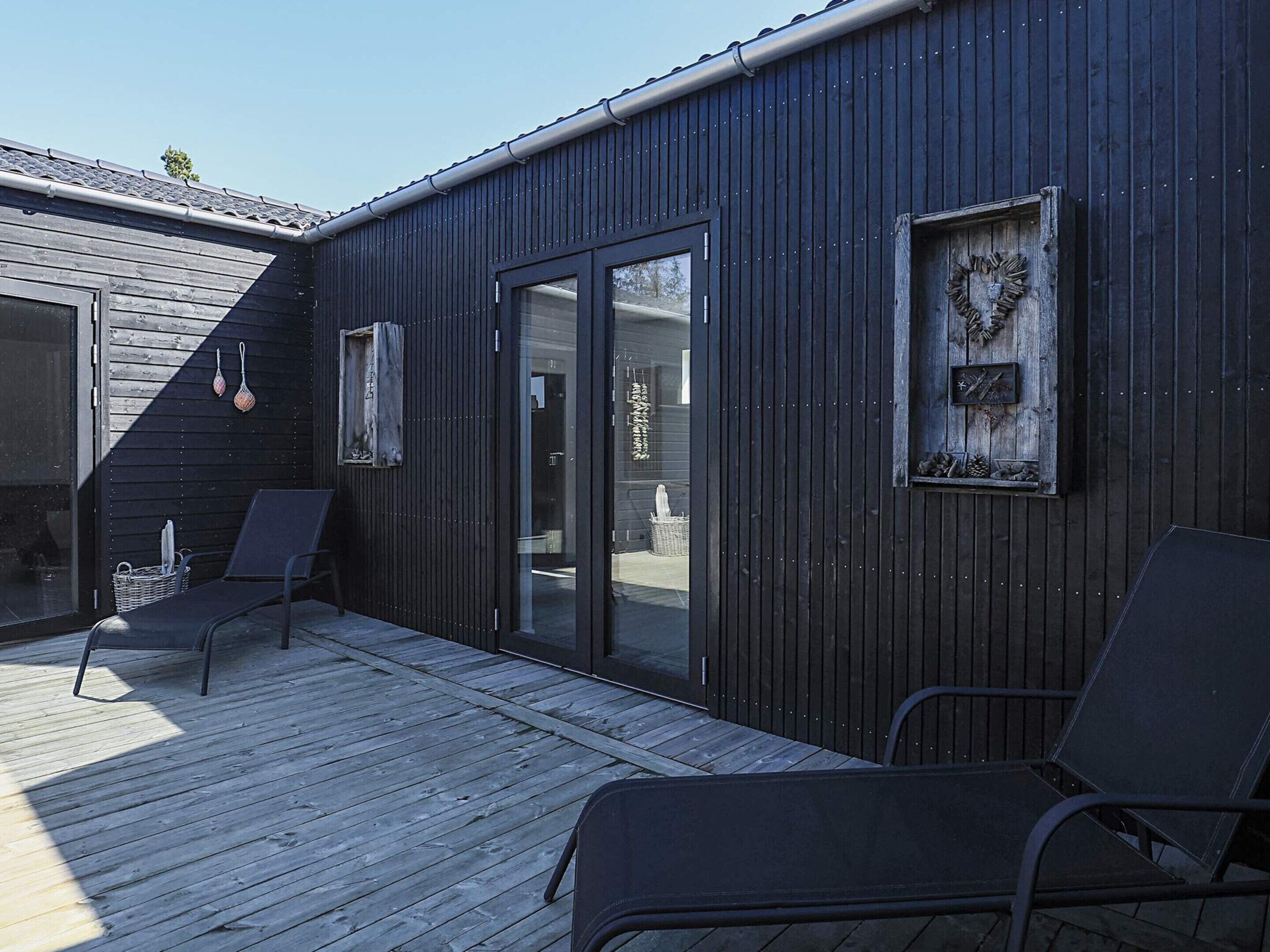 Un bâtiment moderne à l’extérieur sombre, doté d’une terrasse en bois et de deux chaises longues.