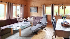 En hyggelig stue med sofa, lænestol og sofabord, trægulve og store vinduer med gardiner.