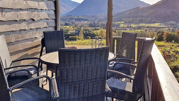 En balkon med fletstole og et bord med udsigt over et bjergrigt landskab.