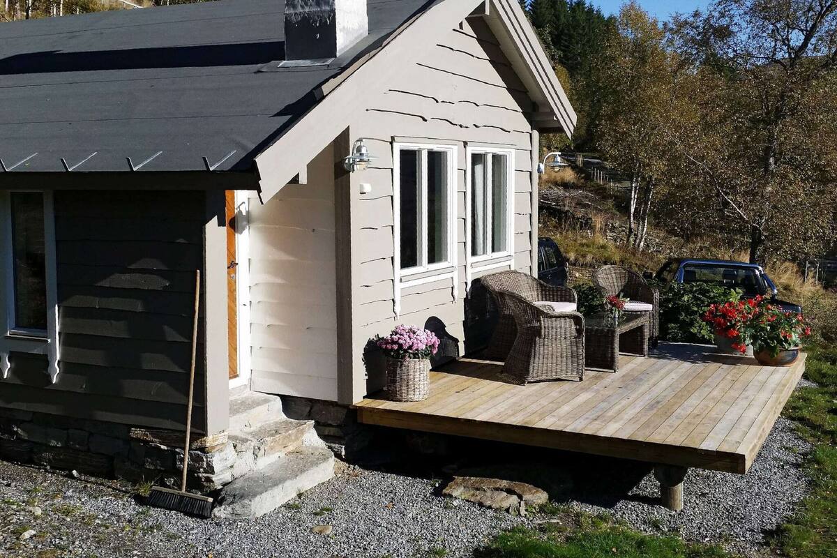 A small cabin with a wooden deck, wicker furniture, and a vehicle parked nearby.