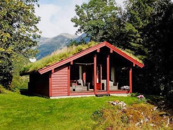 A small red cabin with a sloped roof, situated on a grassy hill with a mountain backdrop. - 6 Person Holiday Home in Olden (Stryn)