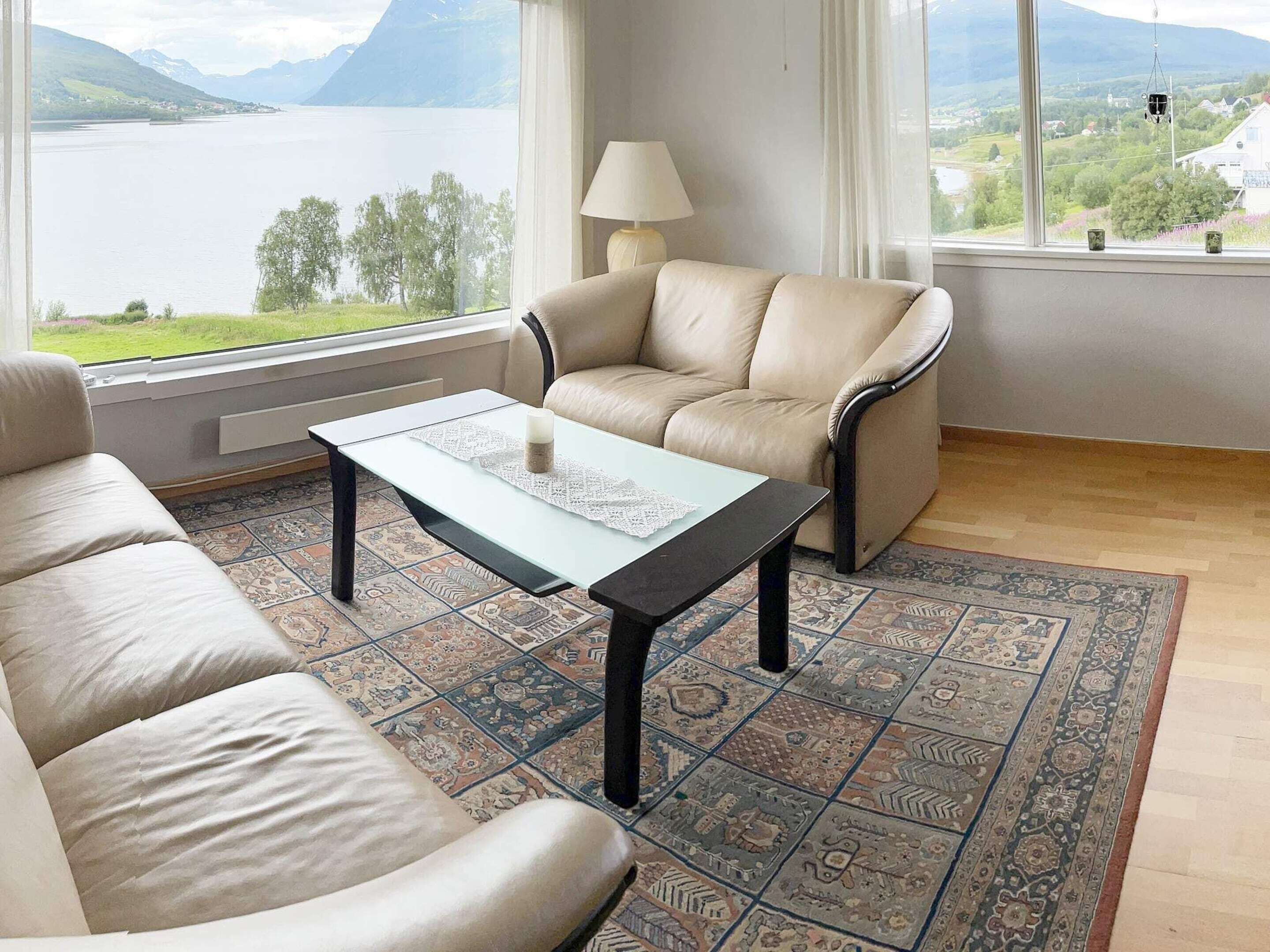 Ein Wohnzimmer mit einer Couch, einem Couchtisch und Blick auf einen See und Berge.