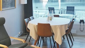 Un espace repas comprenant une table ronde, des chaises et une vue sur un plan d’eau et des bâtiments.