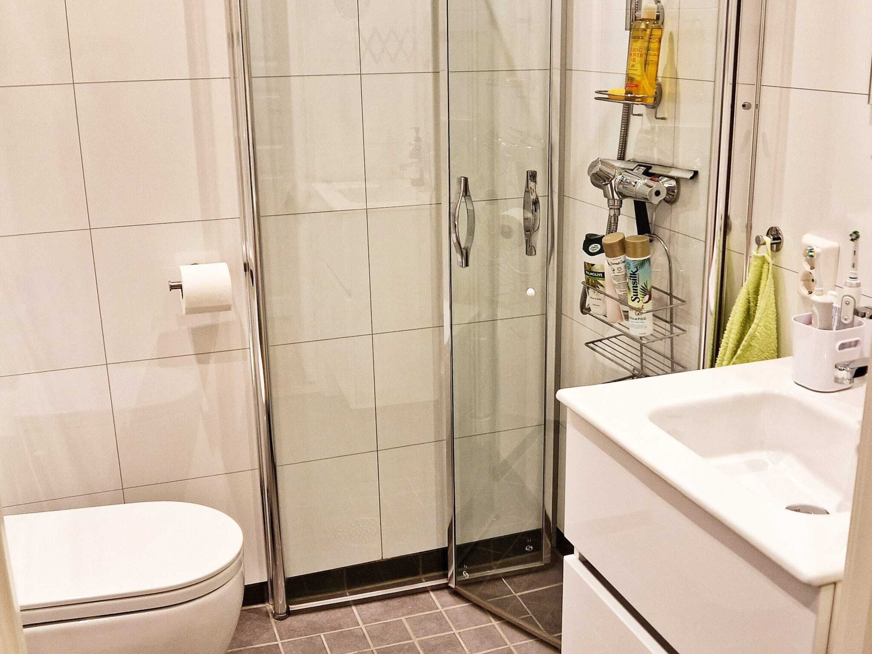 A bathroom with a toilet, a glass shower enclosure, and a sink with toiletries.