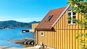 Een houten huis aan een meer, met een helder uitzicht op het water en heuvels op de achtergrond.