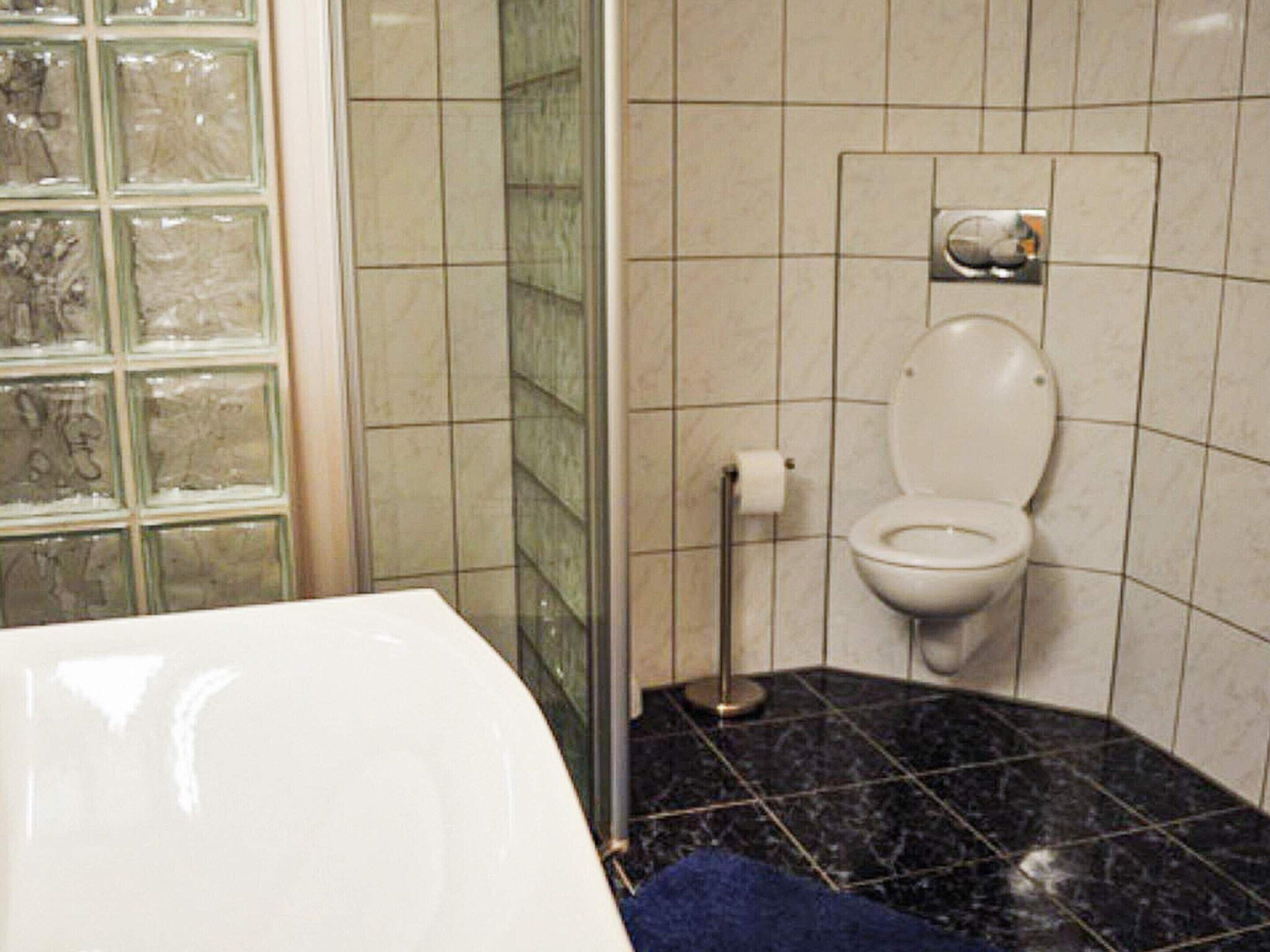 A bathroom with a toilet, a glass shower enclosure, and a marble floor.
