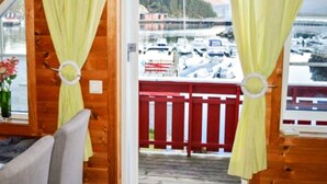 Een chalet met houten inrichting, een balkon met rode leuning en uitzicht op boten en een bebost gebied.