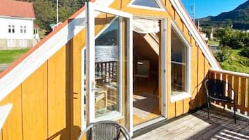 A wooden cabin with a glass door leading to a room with a bed and a chair.