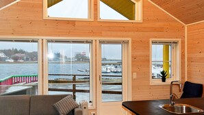 Een gezellig houten vakantiehuisje, met een bank, een klein tafeltje, een keukenhoek met een spoelbak en grote ramen met uitzicht op een besneeuwd water.