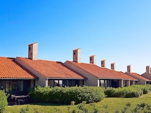 A row of modern buildings with red-tiled roofs and brick walls, surrounded by green shrubbery.