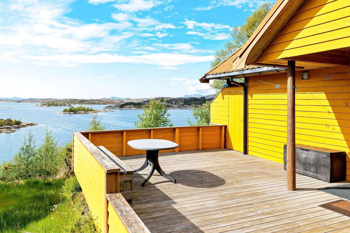 A wooden deck with a table and chairs, overlooking a body of water and hills.