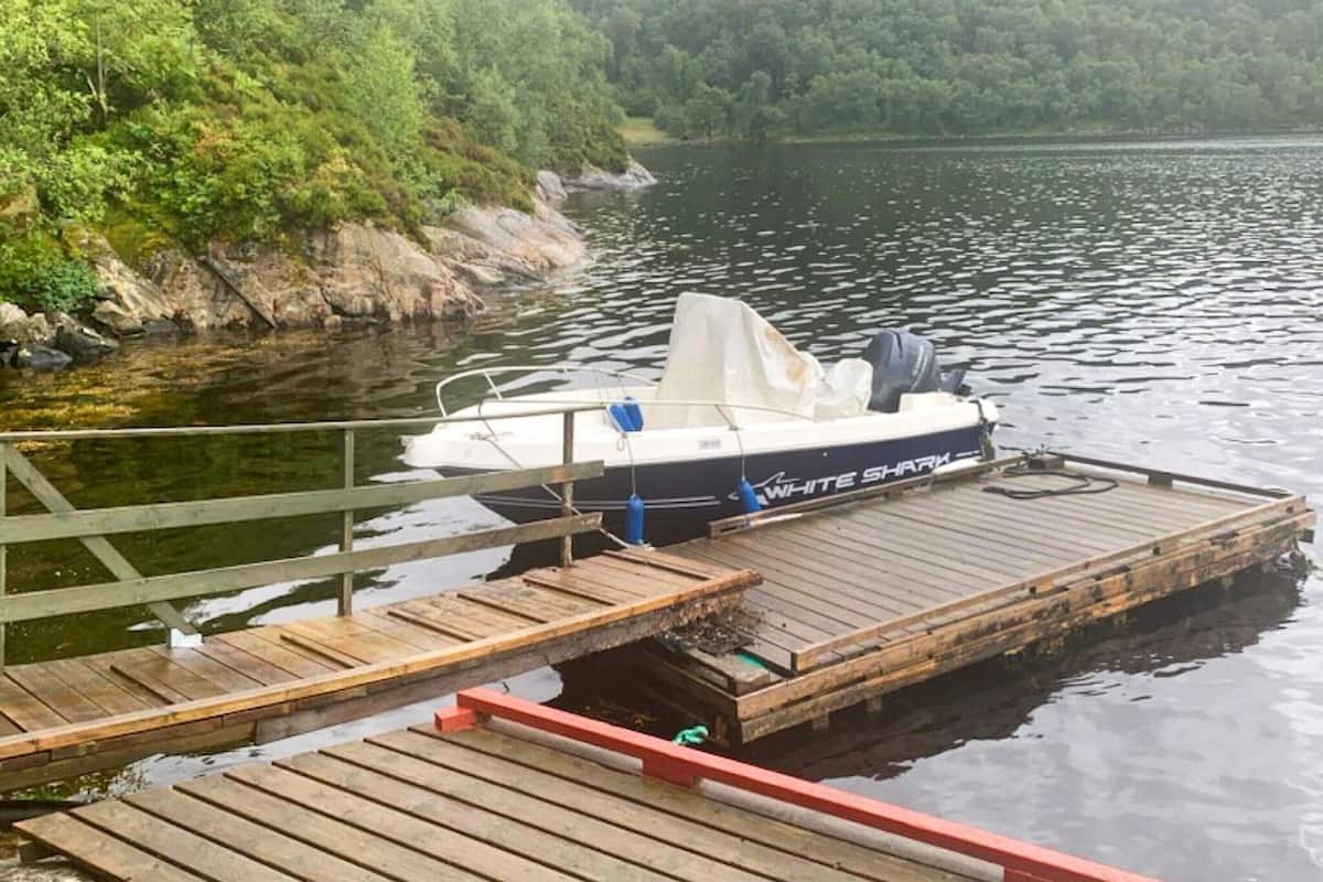 A boat named "White Shark" docked at a wooden pier with a forested shoreline in the background.