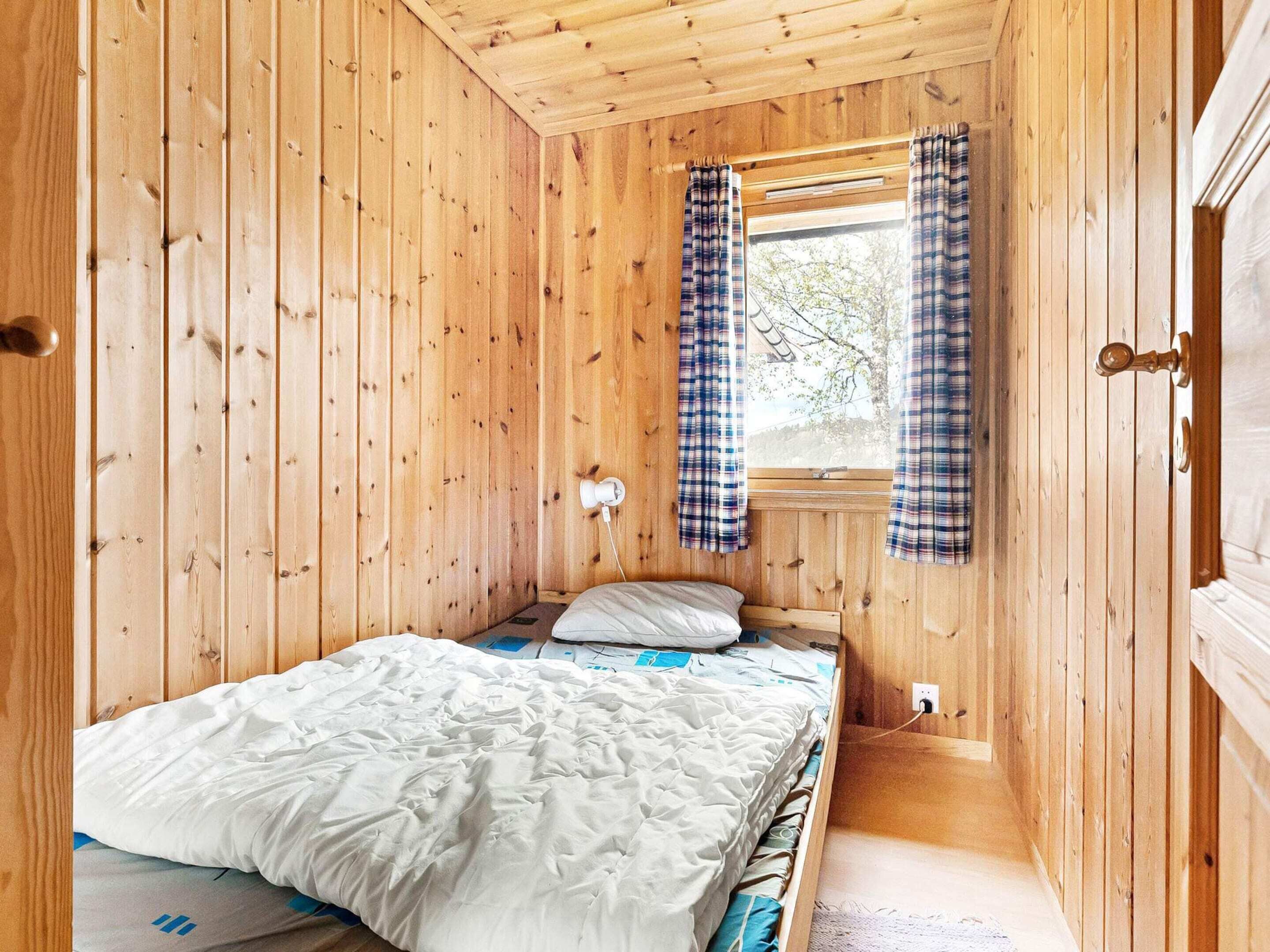 Une pièce en bois avec un lit, une fenêtre avec des rideaux et une porte.