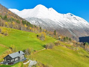 A house with a dark roof and a large front porch, surrounded by a green field and a snow-capped mountain in the background. - 8 Person Holiday Home in Valldal (Fjord)