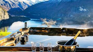A table with a champagne bottle, glasses, and a bucket, overlooking a mountainous landscape with a lake.