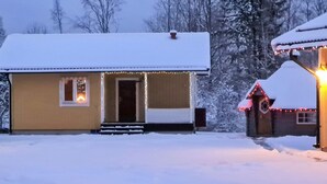 A snow-covered house with a porch and a small shed with lights.