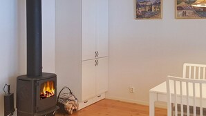 A room with a wood-burning stove, white cabinets, a white chair, and two paintings on the wall.