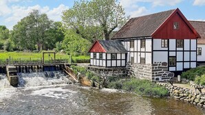 A traditional half-timbered house with a red roof and a small water mill structure beside a flowing river.