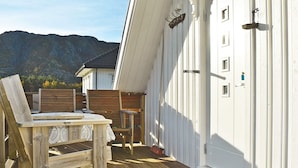 A wooden deck with a table and chairs, a white door with a window, and a mountain in the background. - 4 Person Holiday Home in Oksvoll (Orland)