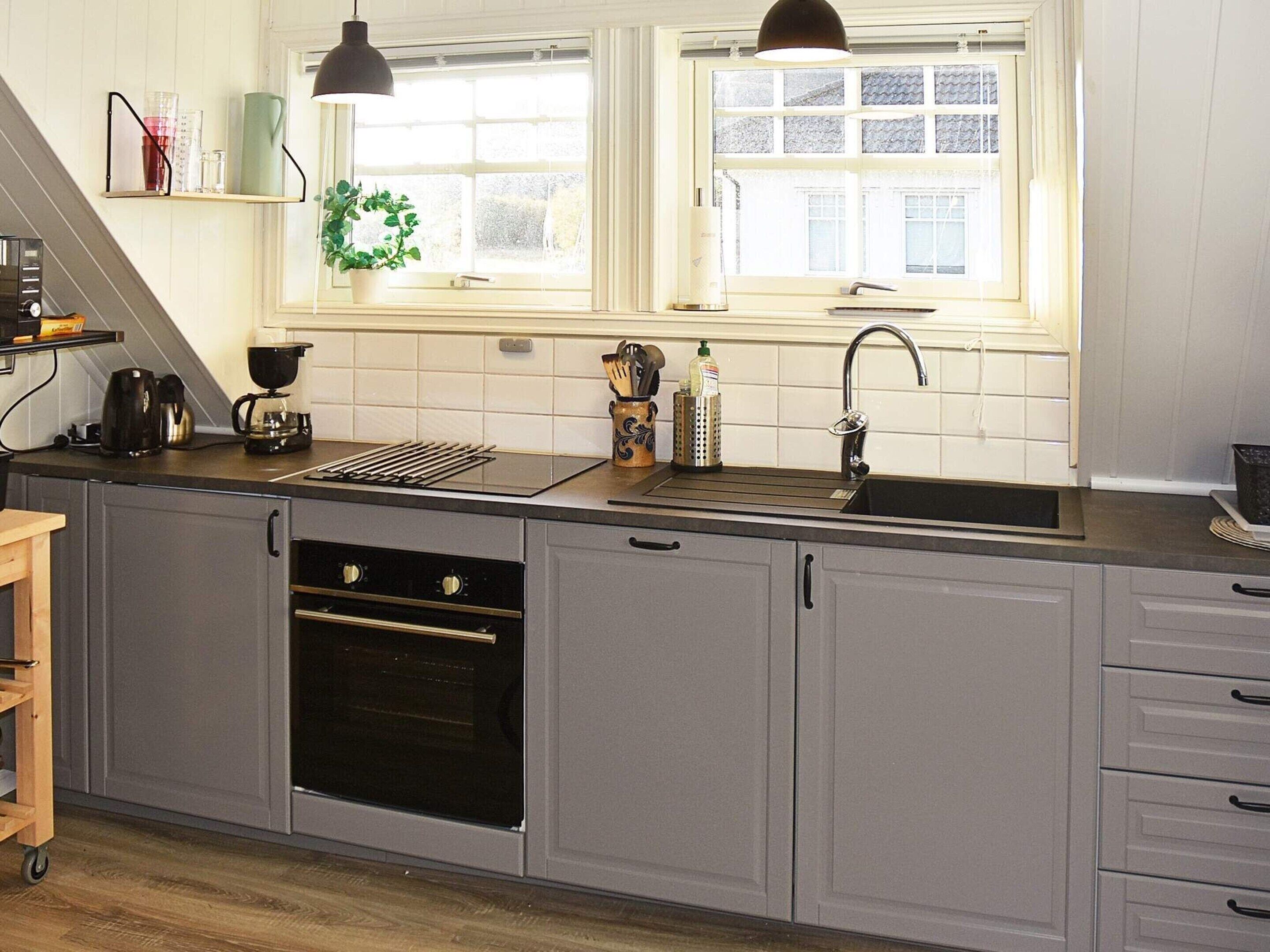 A modern kitchen with grey cabinets, a black stove, a sink, and a window above the sink.