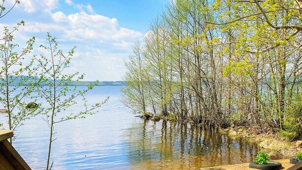 A lakeside view with a wooden deck and a sandy area with tire planters. - 4 Person Holiday Home in Braas (Braås)