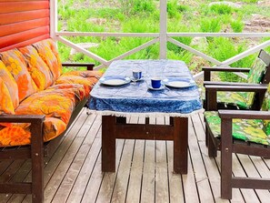 Une terrasse en bois avec une table bleue dressée pour deux personnes, entourée de chaises en bois.