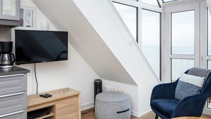 Un dormitorio tipo loft moderno con un tragaluz grande, un televisor, una cafetera, un pequeño otoman y un sillón azul.
