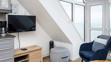 A modern loft bedroom with a large skylight, a television, a coffee maker, a small ottoman, and a blue armchair.