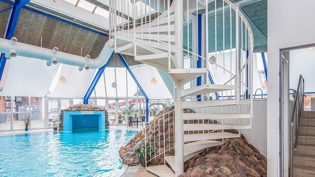 Una piscina interior con pared de piedra y una escalera espiral blanca.