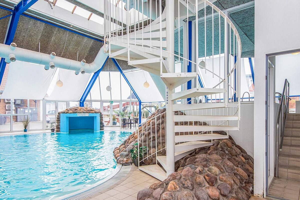 Ein Innenpool mit Steinwand, einer weißen Treppe und blauer Decke.
