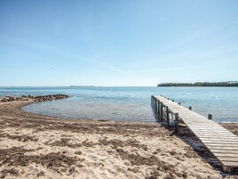 Un molo in legno si protende in acque calme, circondato da una spiaggia sabbiosa con alghe.